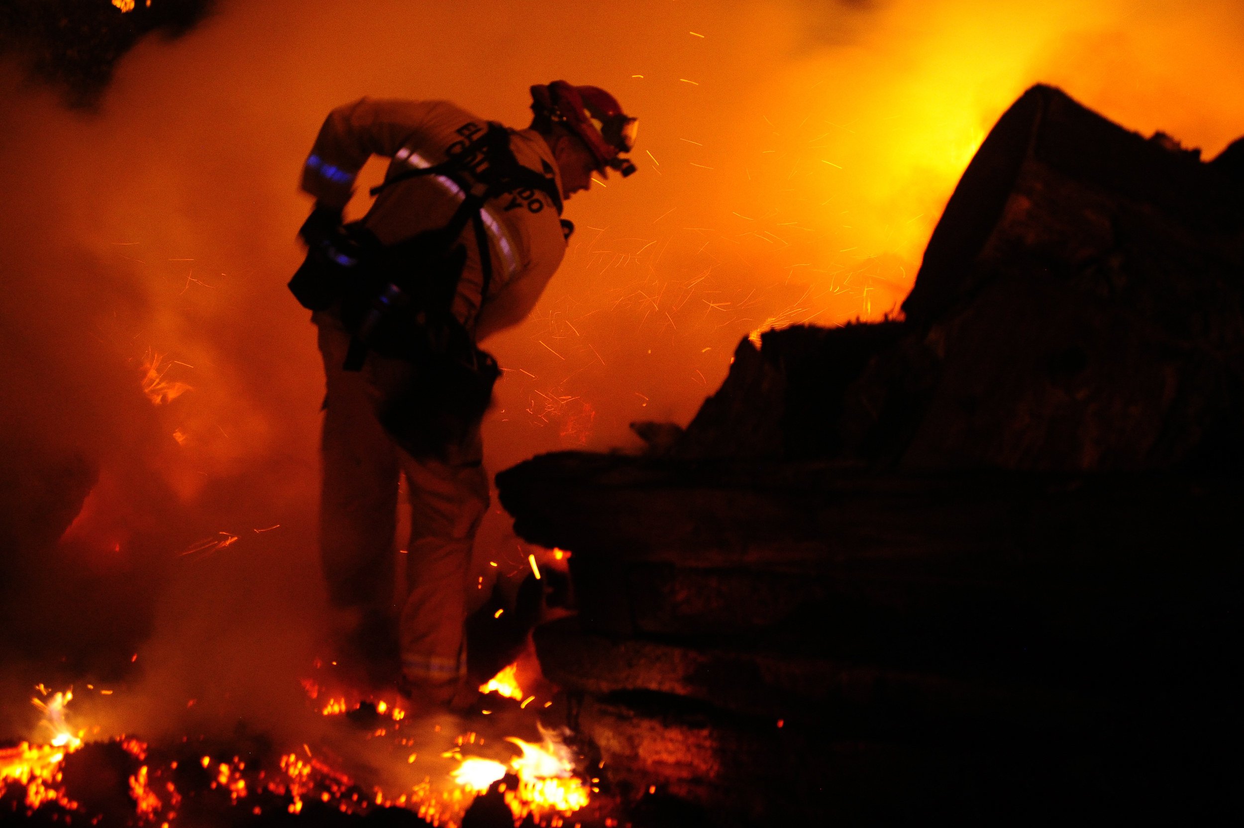 A firefighter stands on burning embers at night