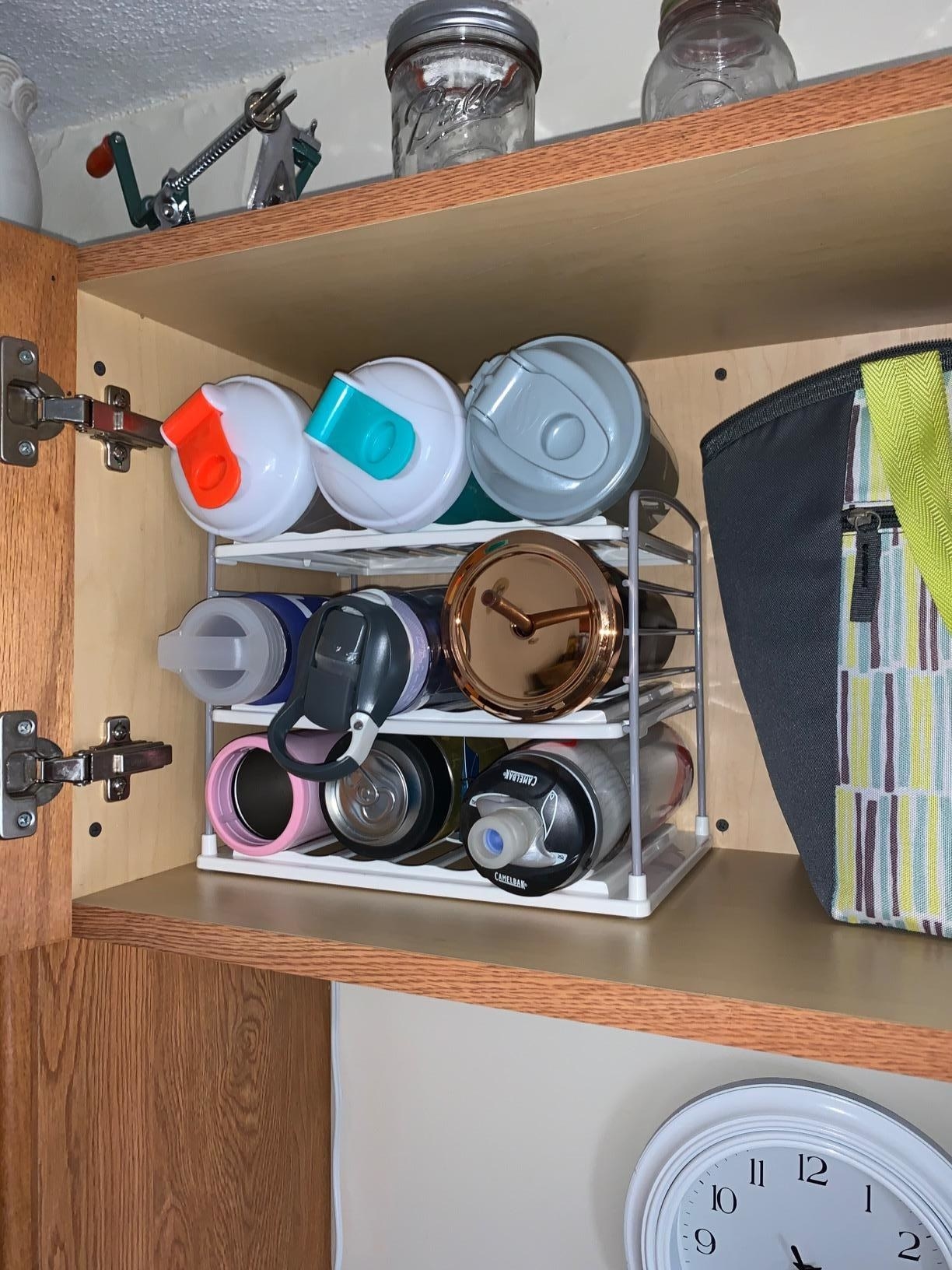 reviewer image of nine water bottles neatly organized on the water bottle organizer in a cabinet