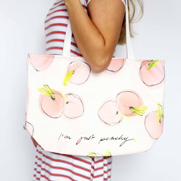 model holding large tote that reads &quot;i&#x27;m just peachy&quot; with peaches printed on it