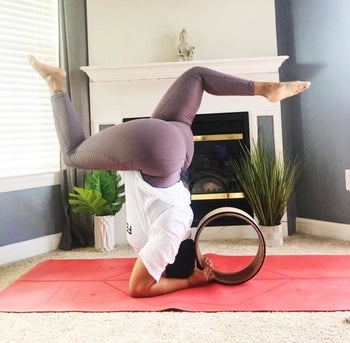 reviewer in headstand position with a brown yoga wheel