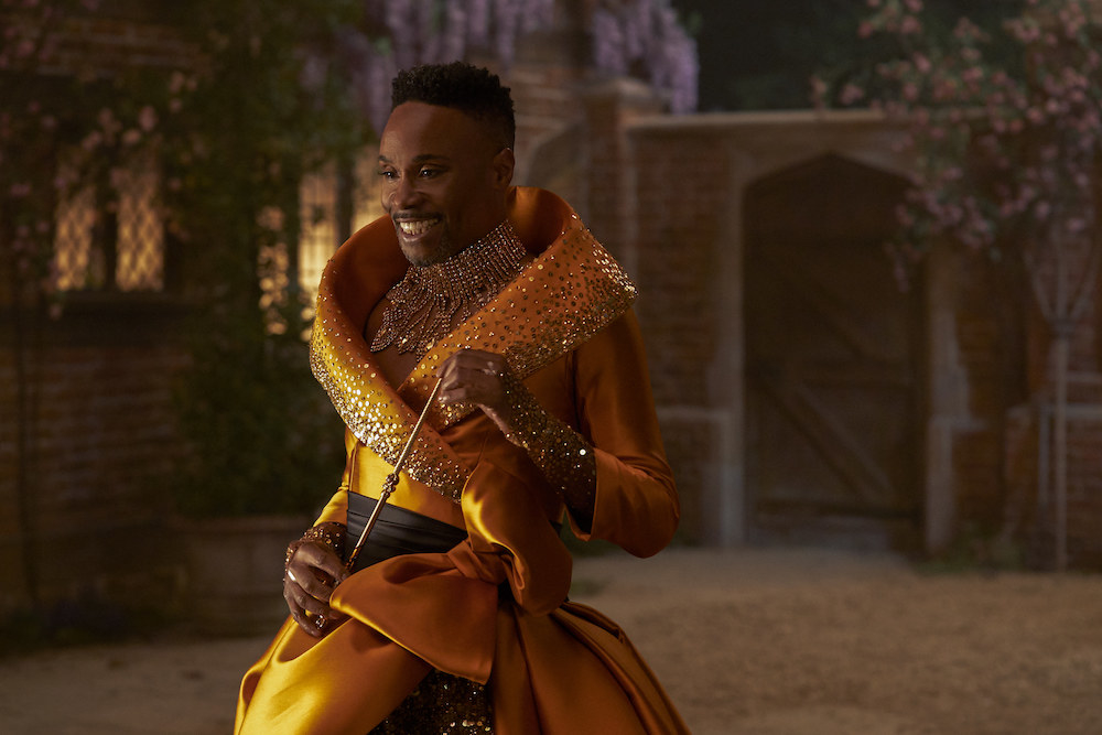 Billy Porter in a gown made from bright orange, satin material, with stunning jewelry and a wand