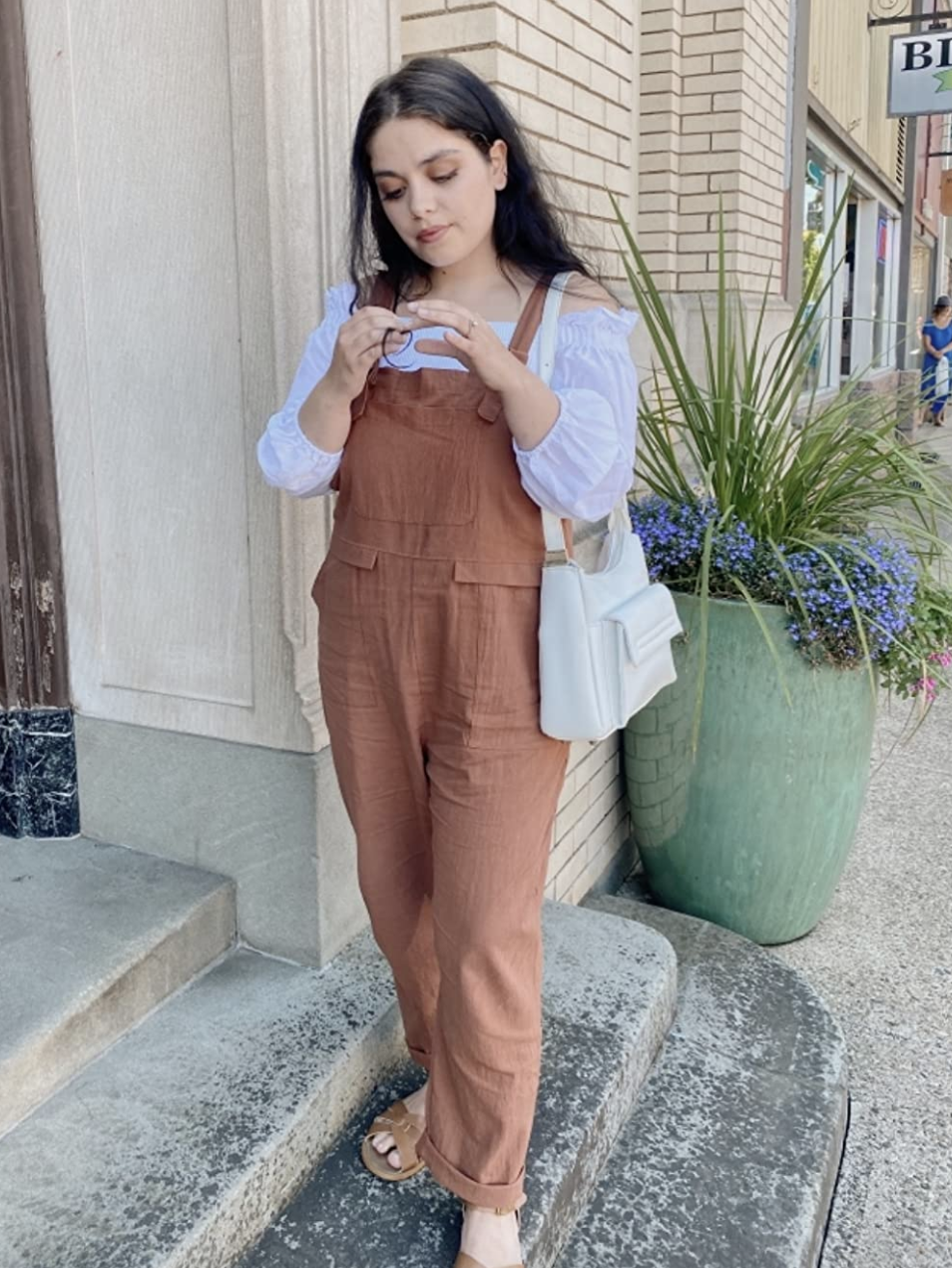 reviewer wearing the brown jumpsuit over a white off-the-shoulder top