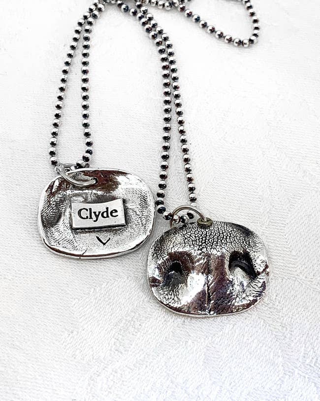 silver necklace on a chain with a 3D dog nose and the dog's name on the other side