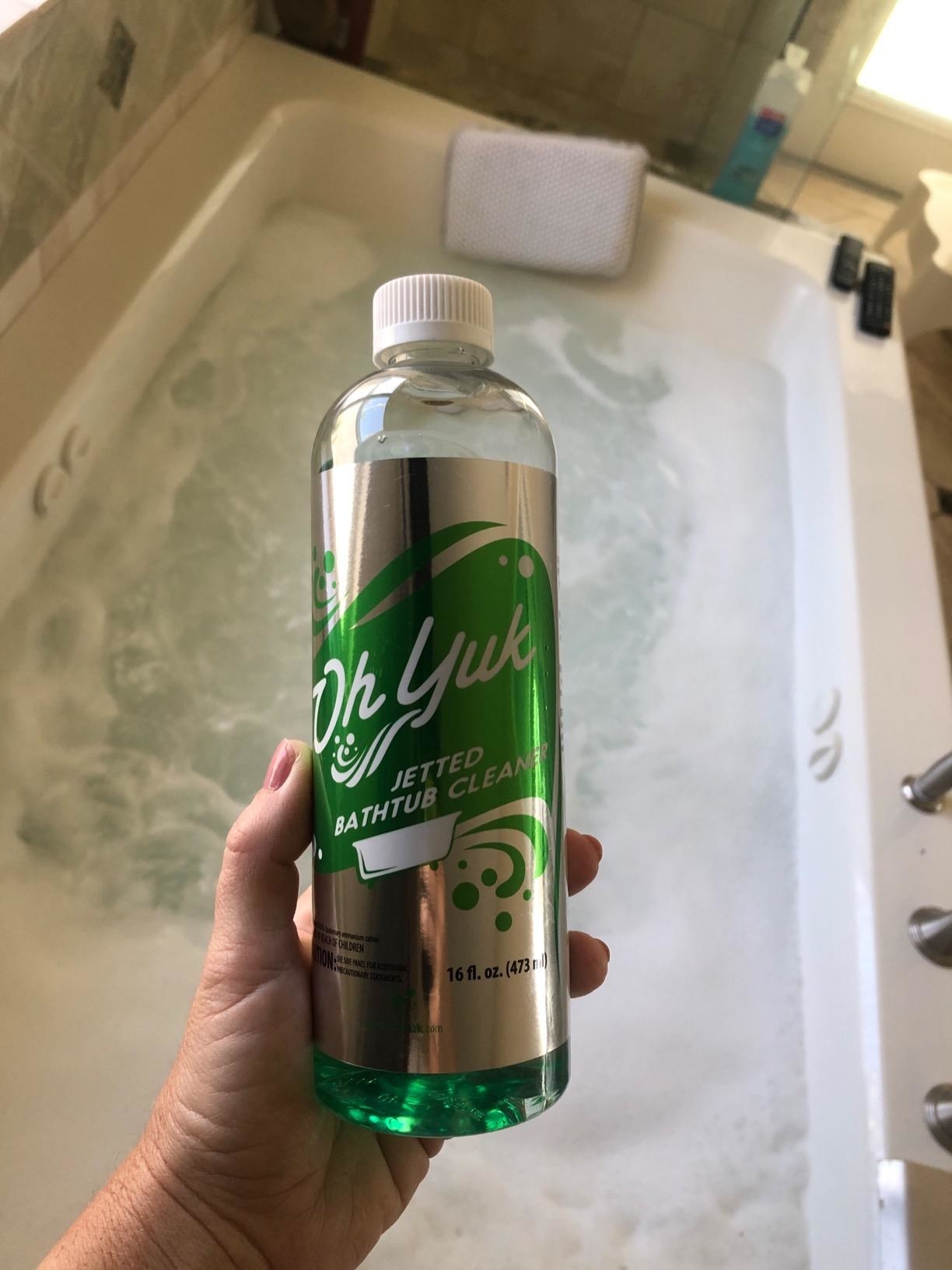 hand holds bottle of the cleaner above foamy jacuzzi getting cleaned