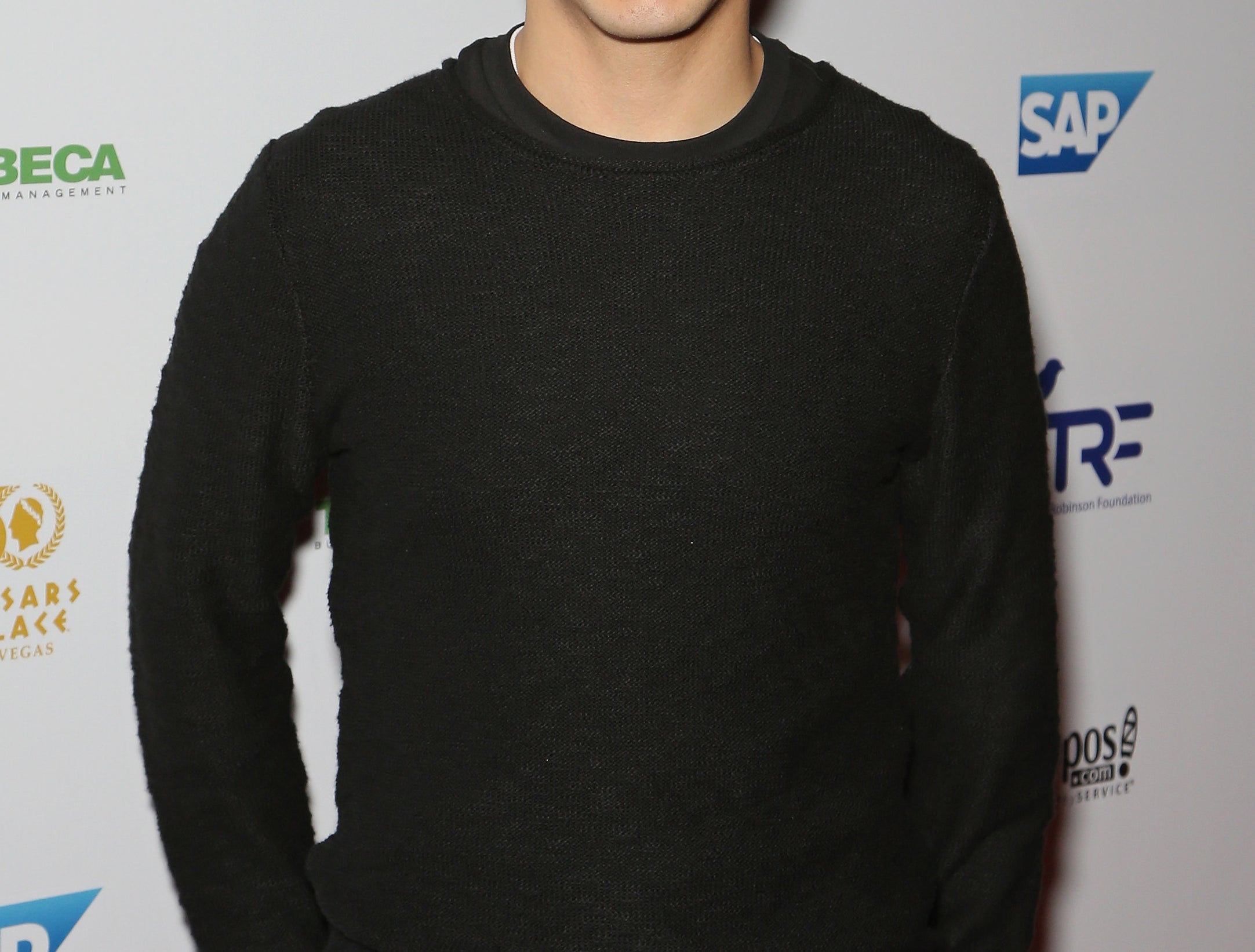 David smiles and wears a plain black long sleeve shirt at an event