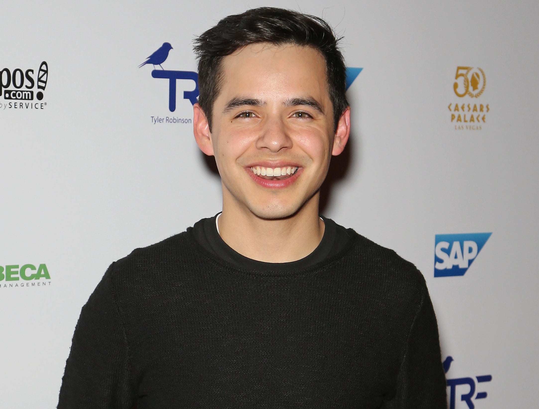 David smiles and wears a plain black long sleeve shirt at an event