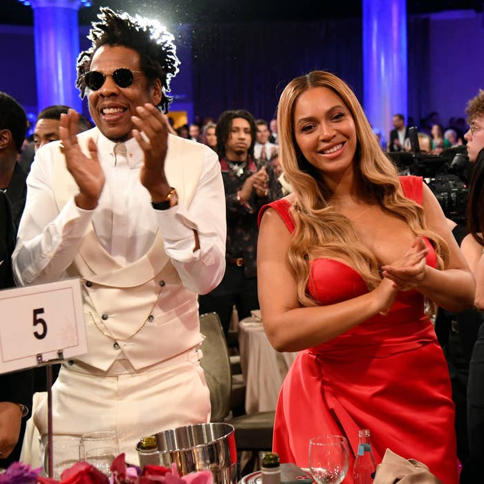 Jay Z and Beyoncé clap while standing up at their table during a pre-Grammy gala