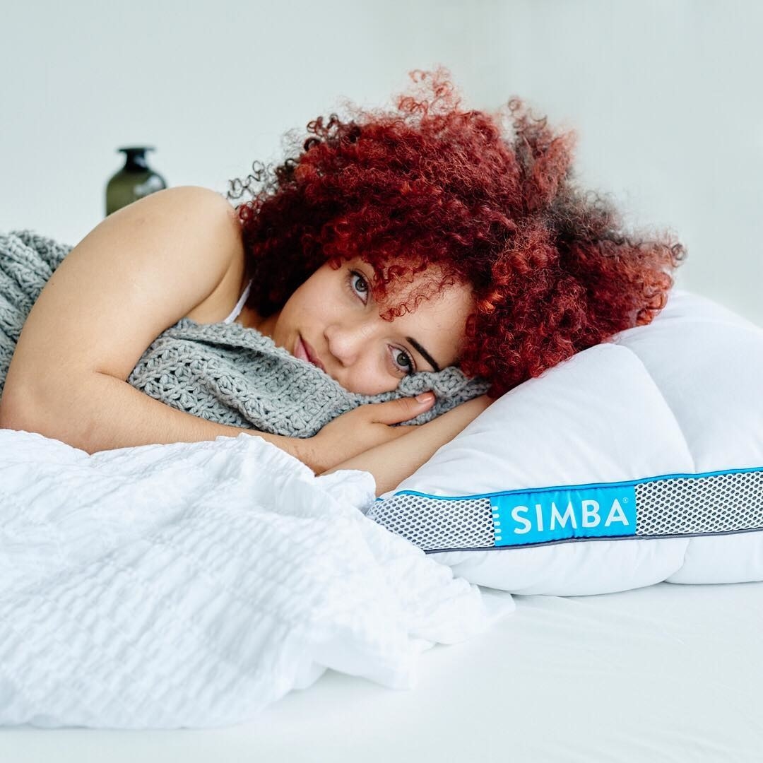 A person looking into the camera while laying on one of the hybrid pillows