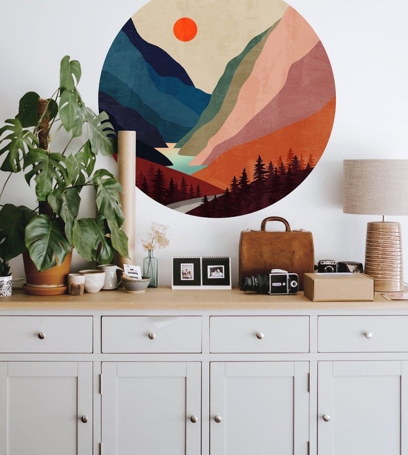 a round, vibrant wall decal with a forest and mountain illustration on a wall above a dresser