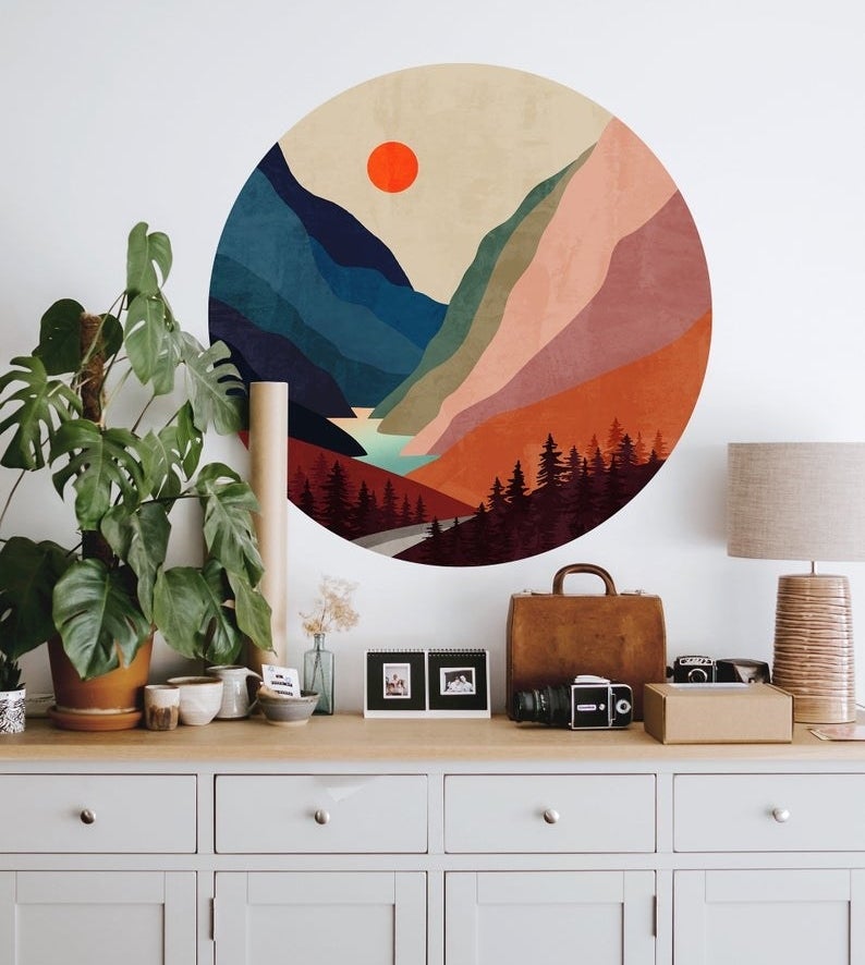 a round, vibrant wall decal with a forest and mountain illustration on a wall above a dresser