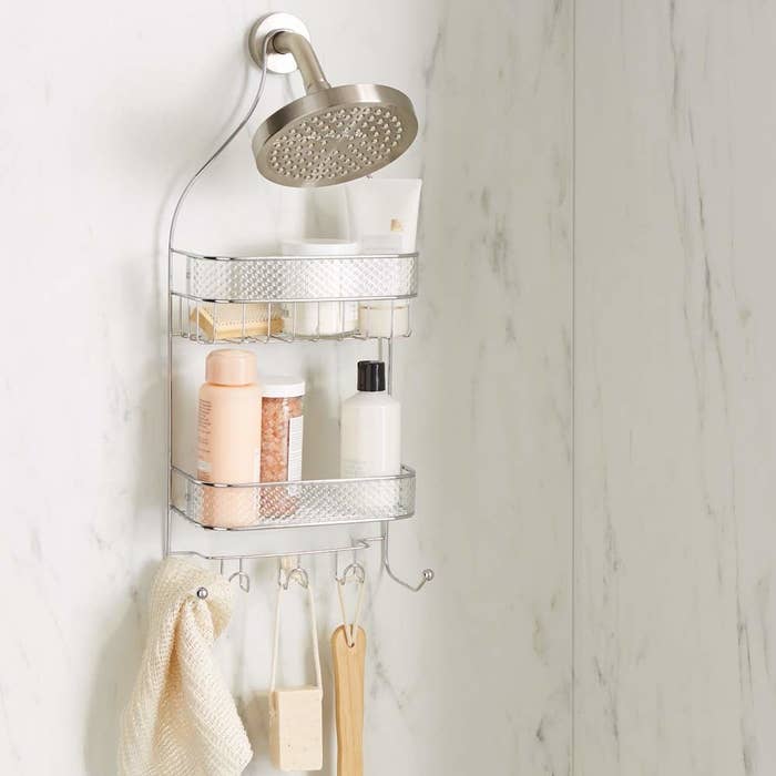 A cage shower caddy with two wire baskets and hooks for hanging storage hung on a shower head