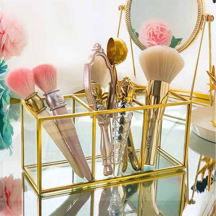 A clear glass bathroom organiser with a golden metal trimmings and 3 compartments