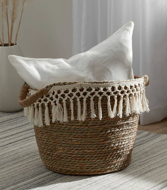a stylish basket with a macrame fringe around the top and a pillow inside