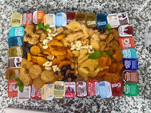 A charcuterie board with chicken nuggets and different sauces