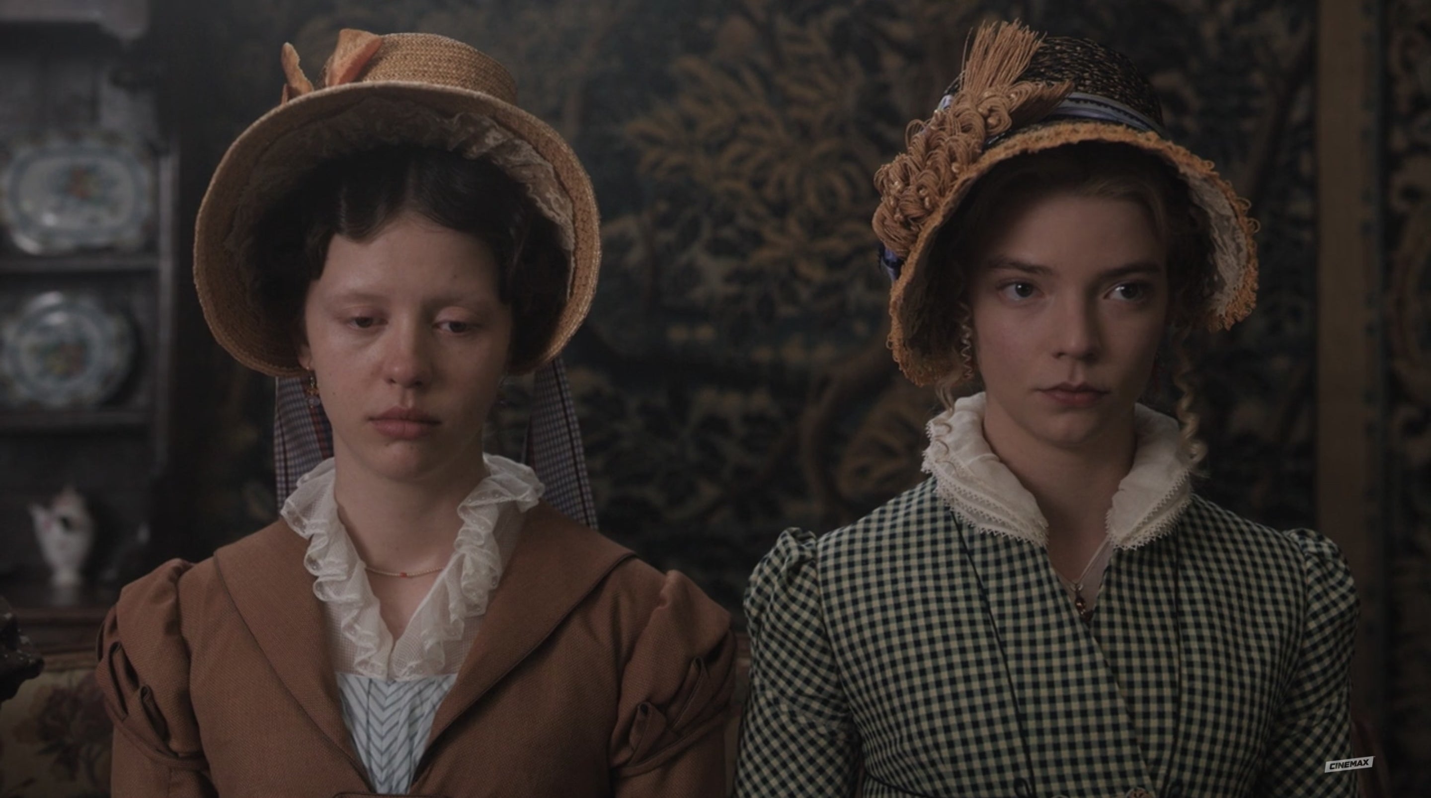 Emma and Harriet stare blankly and bored-looking, each wearing a fancy hat