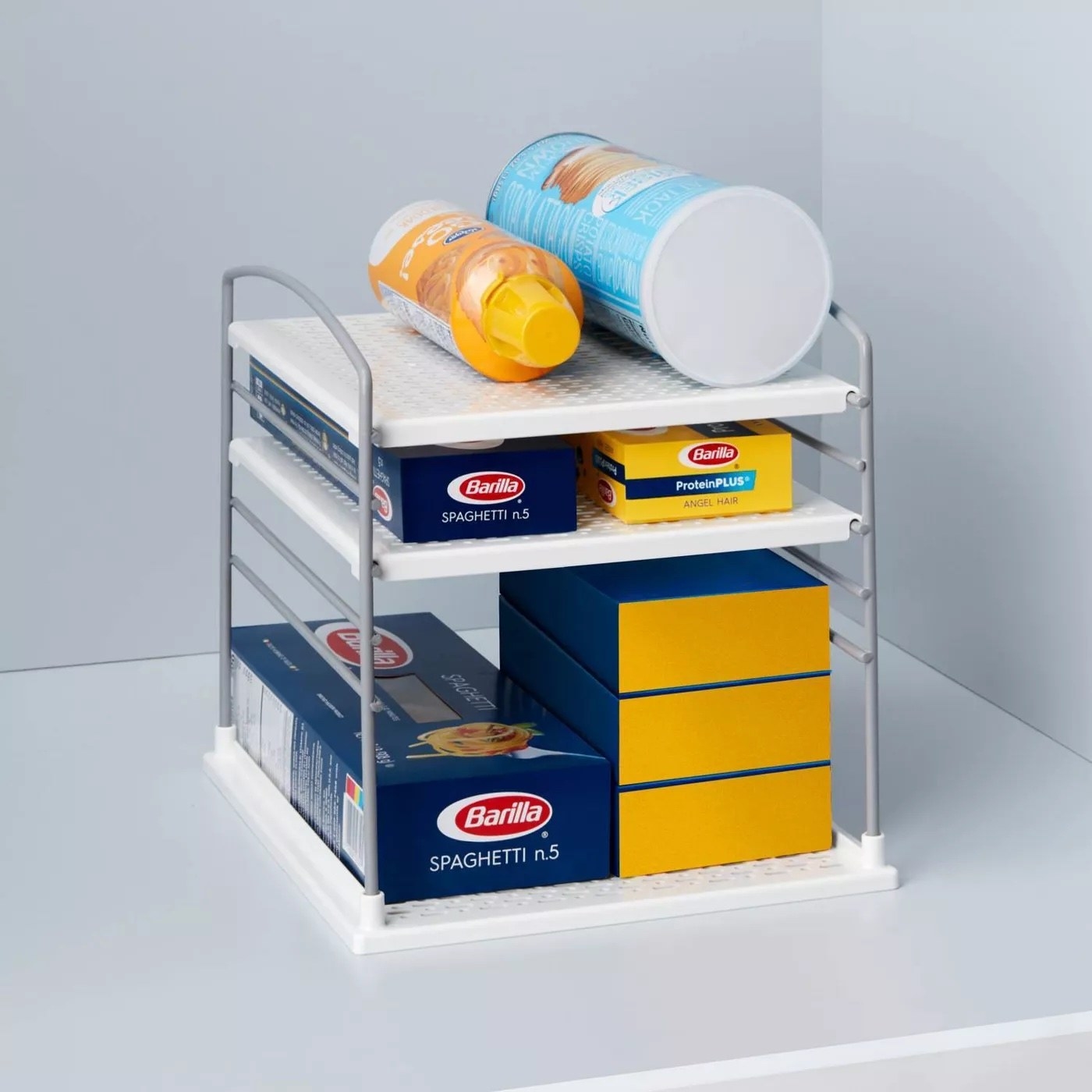 A three-tiered box organizer holding pasta boxes and spray cheese.