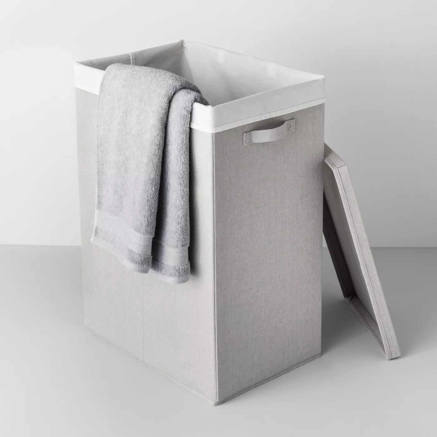 A gray laundry hamper with a gray towel hanging over the lid.