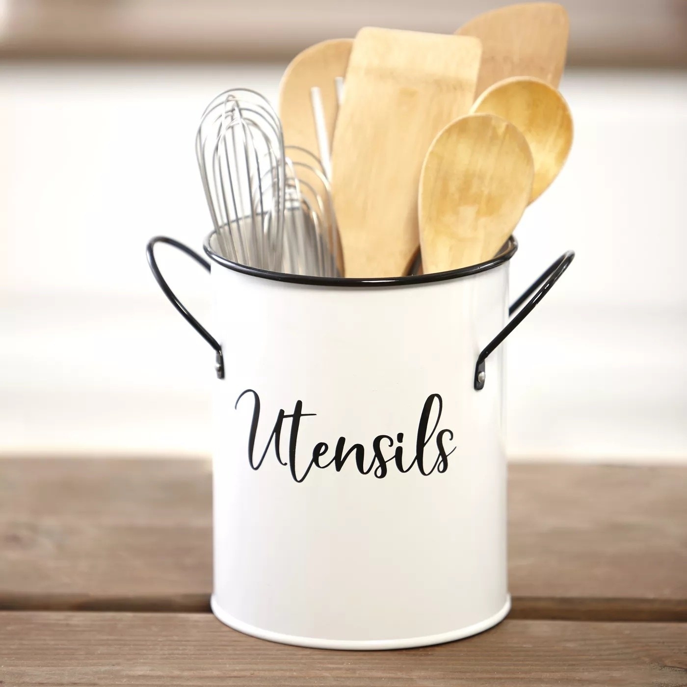 A utensil caddy holden two whisks and wooden spatulas and spoons.