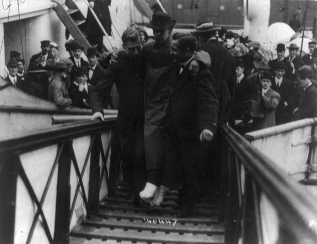 A man with bandaged feet being helped off a boat