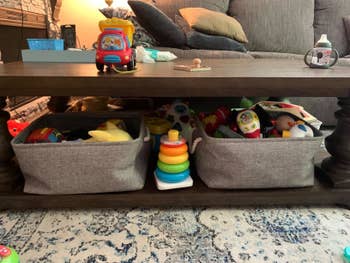 Reviewer's photo showing the grey bins holding toys under their coffee table