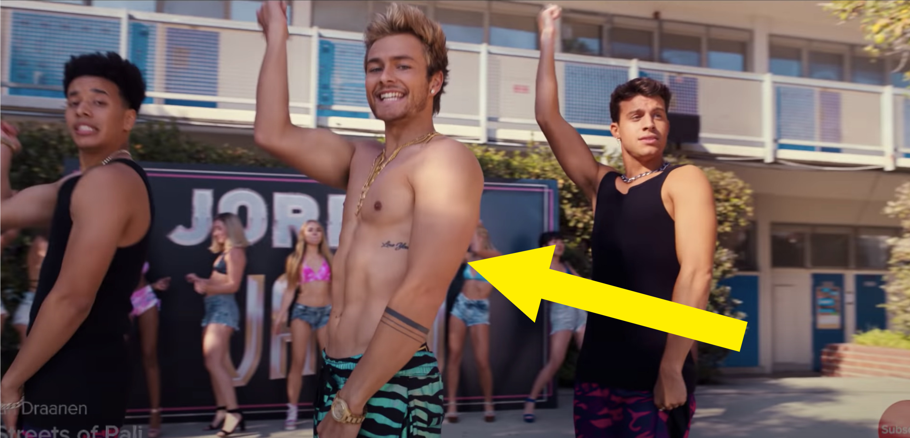 An arrow pointed at a shirtless man seeming doing a choreographed dance with two men