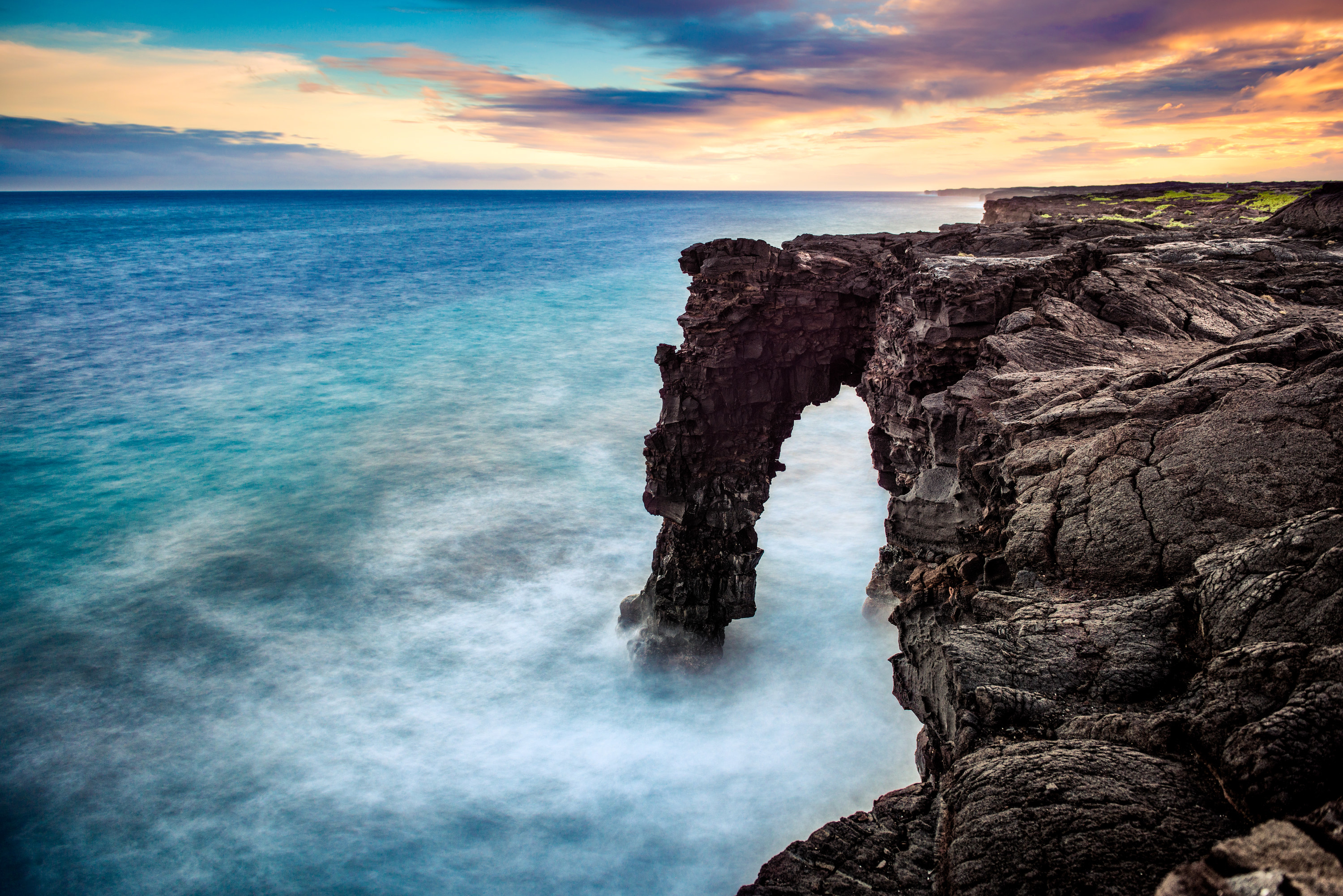Waves crash around a rocky arch that juts out from the Hawai&#x27;i Volcanoes National Park.