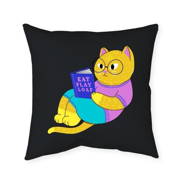 Black square pillow with yellow cat in blue shorts and a magenta shirt holding a book that says &quot;Eat Pray Loaf.&quot; Oh, and it has glasses, and the inside of the ears match the shirt.