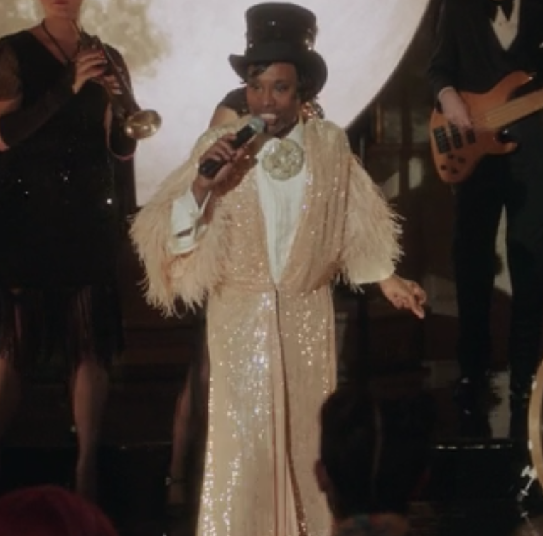 Billy Porter wears a sparkly robe with feathers on the cuffs with a top hat