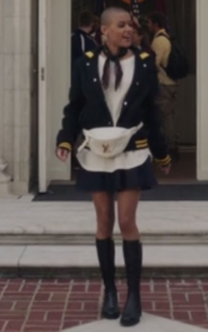 Julien wears a t-shirt tucked into a uniform skirt under a letterman jacket with knee high socks and boots