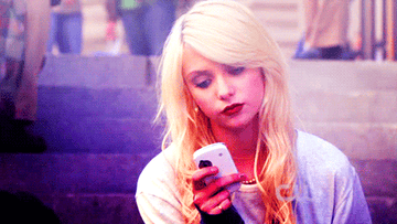 A close up of Jenny Humphrey as she makes an annoyed face as she looks at her cell phone screen