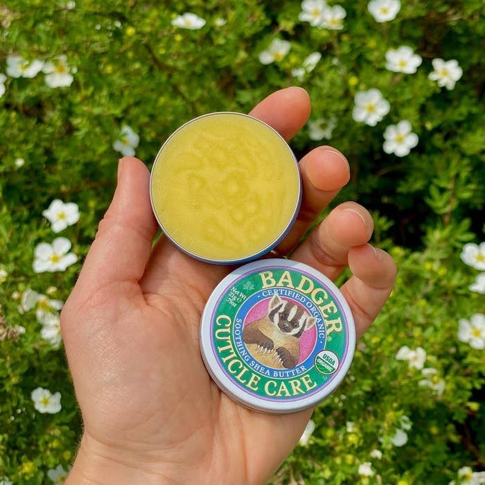 A person holding the balm in front of a flower bush