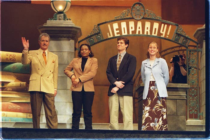 Alex Trebek standing next to three contestants