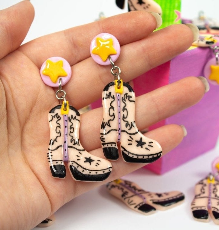 A person holding a pair of the cowboy boot earrings