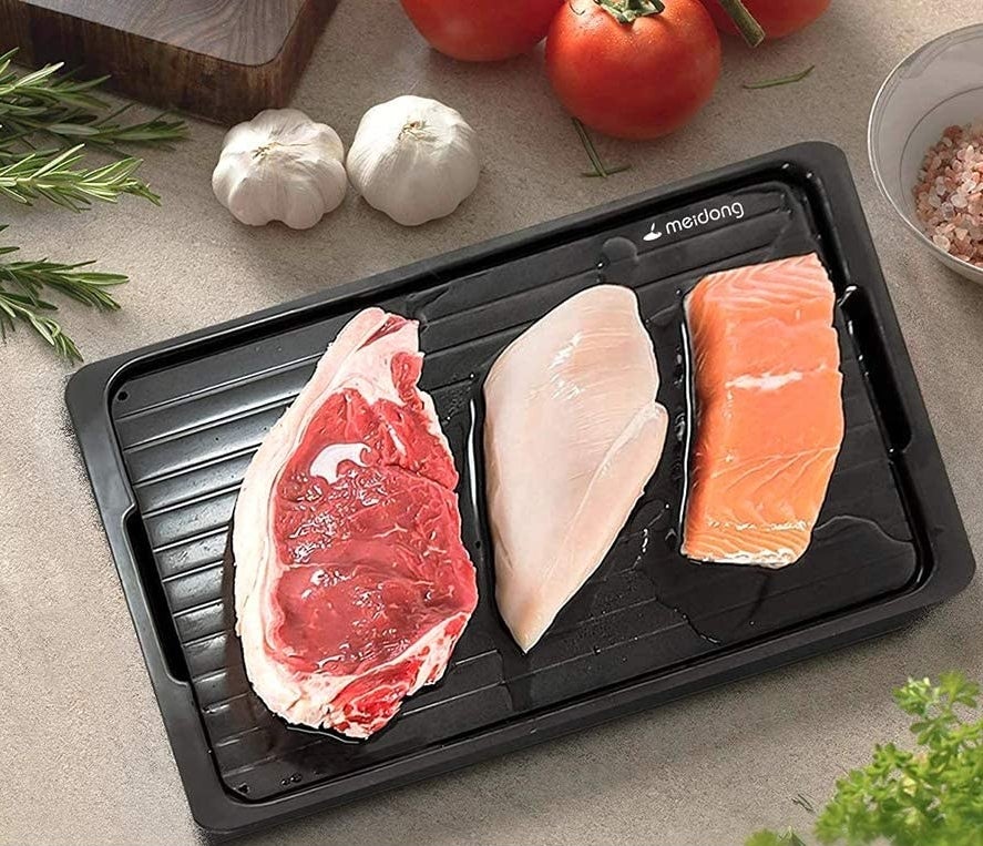 the food thawing tray with a slab of beef, a chicken breast, and a salmon filet defrosting on top