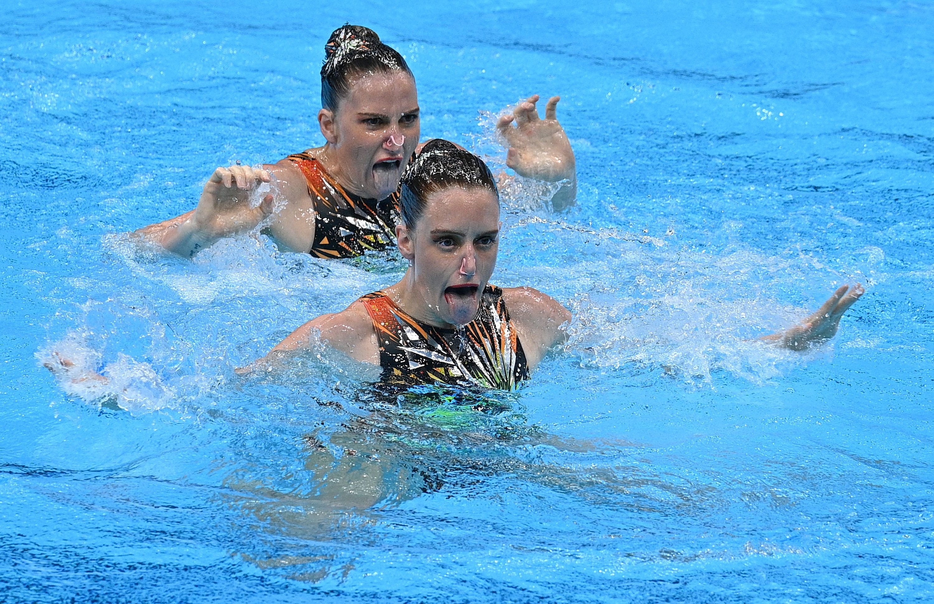 Two women swimmers hold their heads above water in the pool and stick their tongues out at the Tokyo Olympics