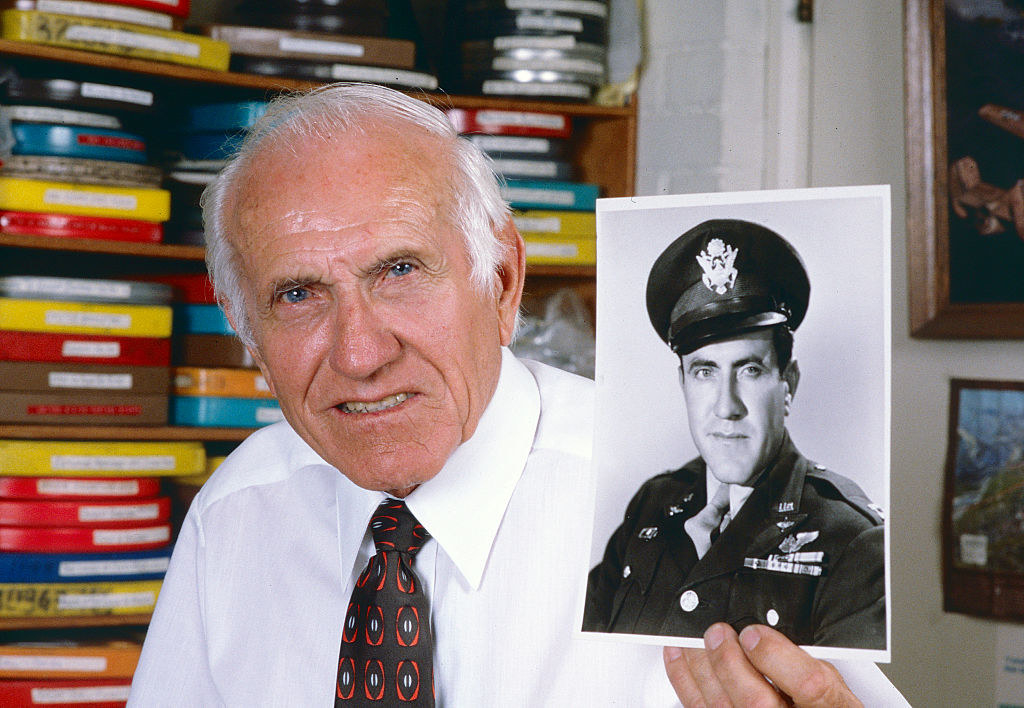 An elderly Louis Zamperini poses with a picture of himself