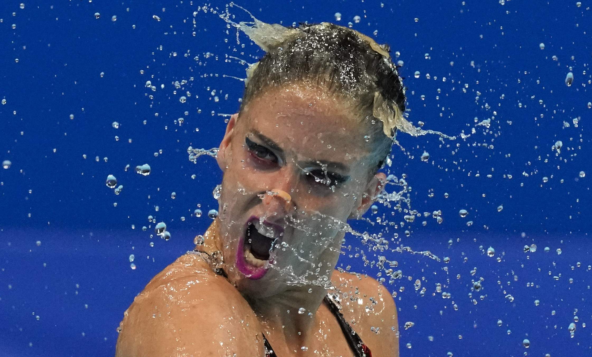 A woman swimmer spins her head, hundreds of droplets of water frozen mid-air around her
