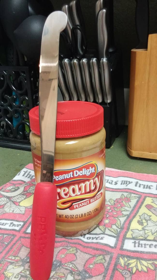 The peanut butter knife with a red handle and curved edge 