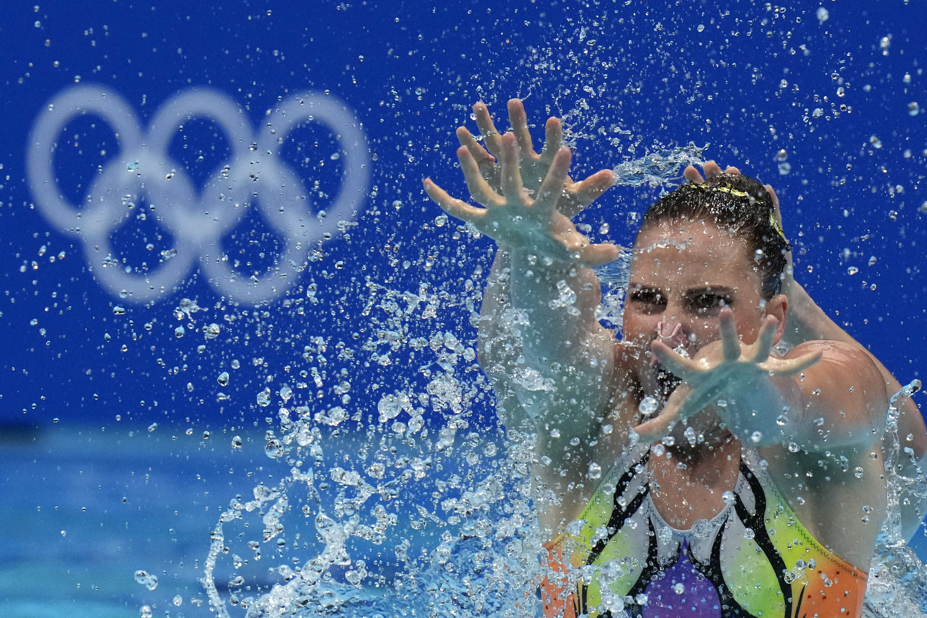 A woman swimmer holds her arms and spread fingers out before her, surrounded by droplets of water