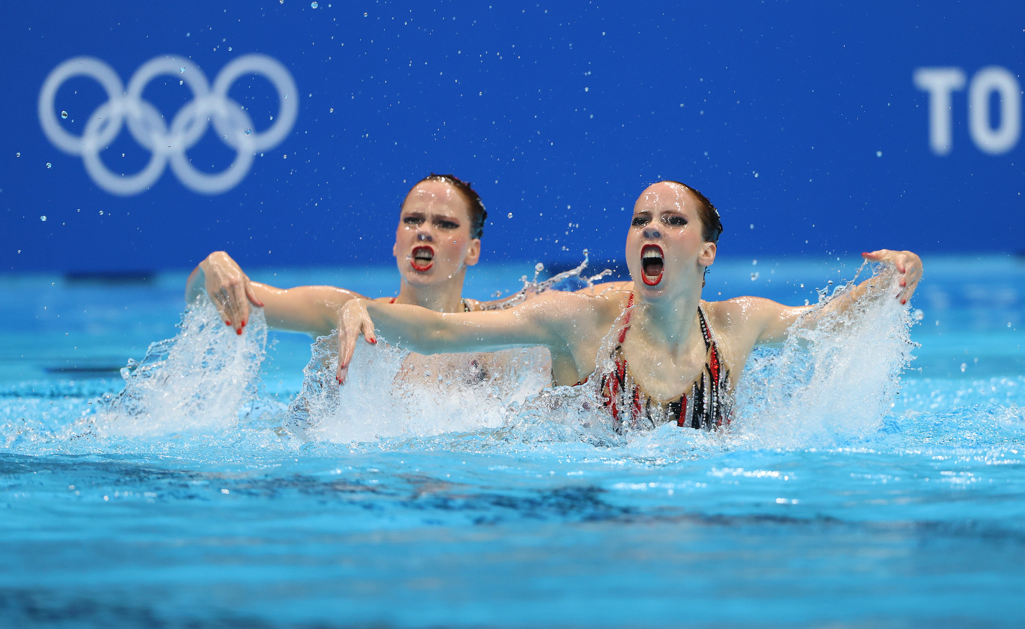 Two women swimmers perform in the pool with their arms to the side