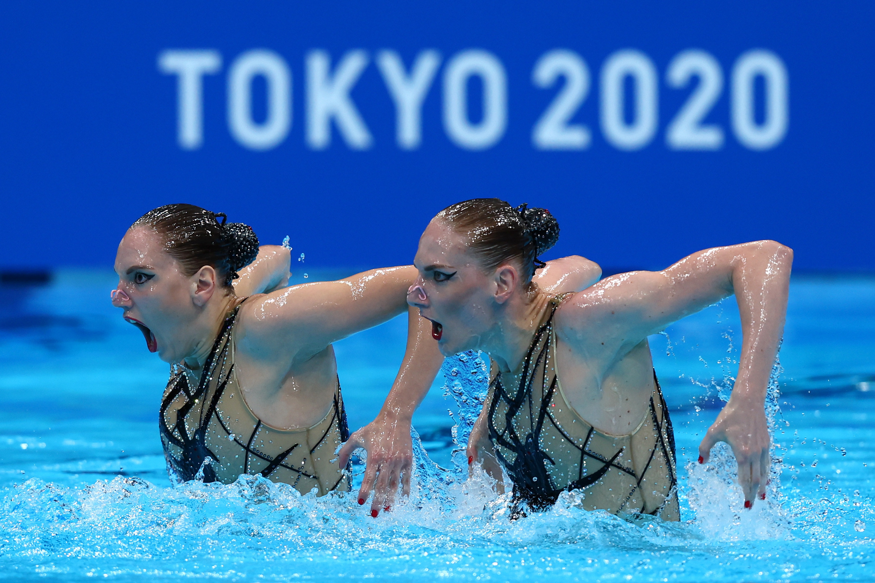 Two swimmers stand side by side with their arms out behind them