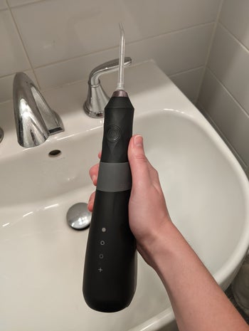 a hand holding the water flosser over a sink 
