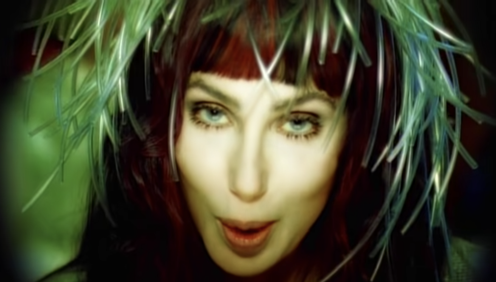 Cher singing in the music video with feathers on her head