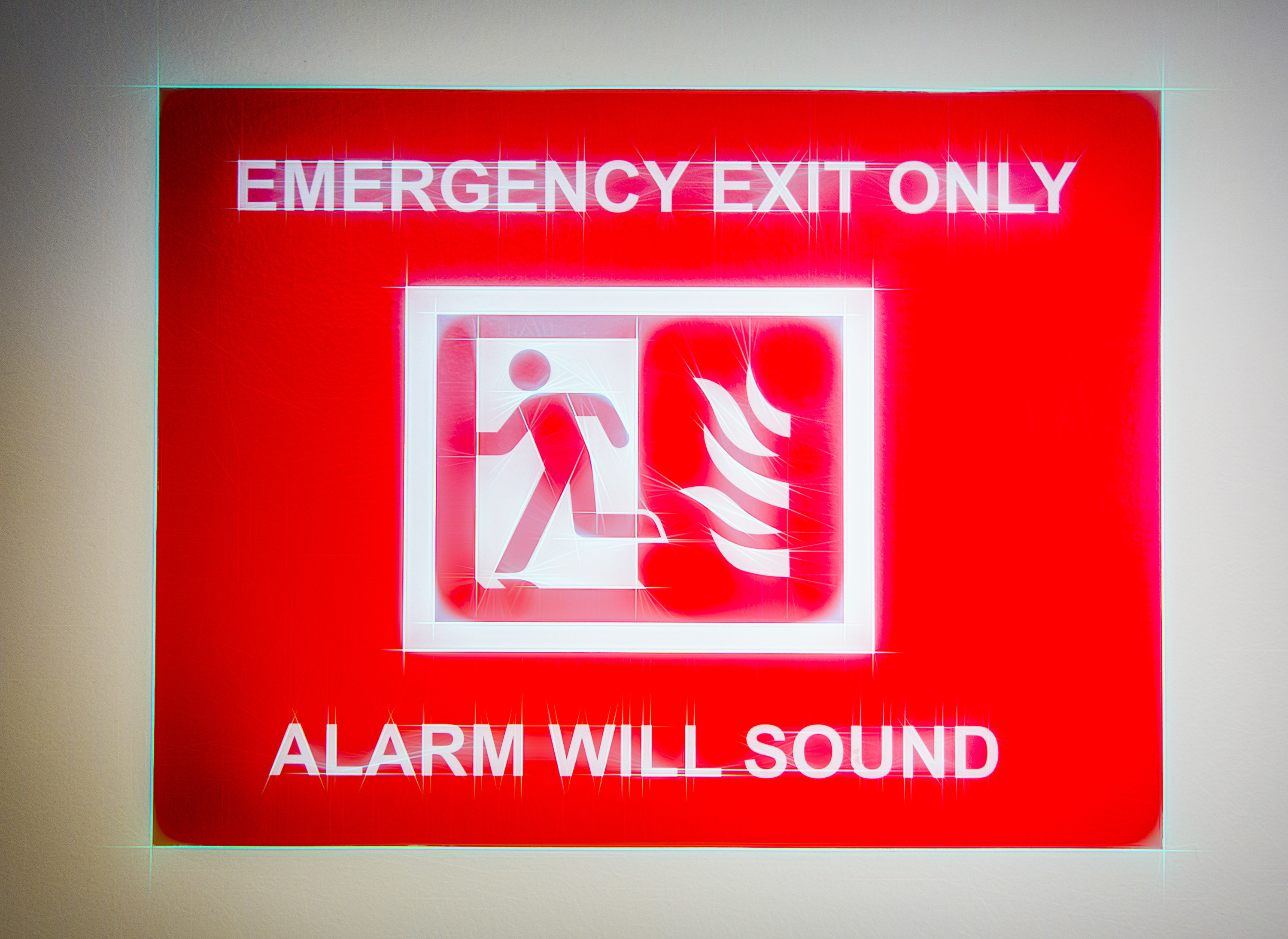Closeup of Emergency Exit sign with text Emergency Exit Only above a diagram of a person running from fire, with Alarm Will Sound text below