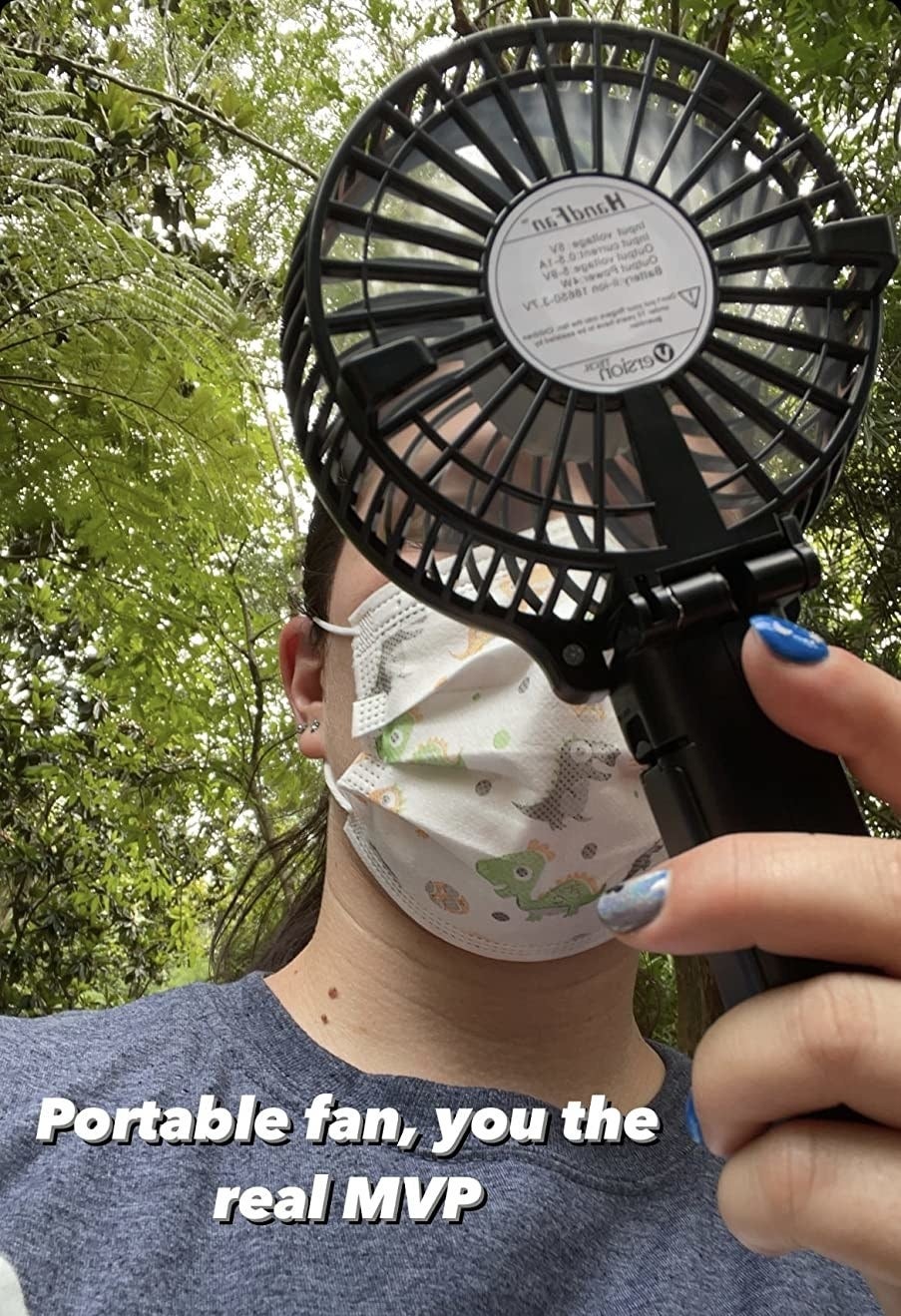reviewer holding the black small fan with the words &quot;portable fan, you the real MVP&quot; on it