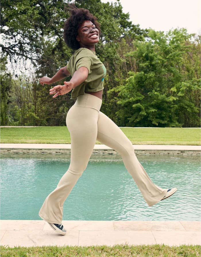 model wearing beige flare leggings and green crop top while walking by the pool