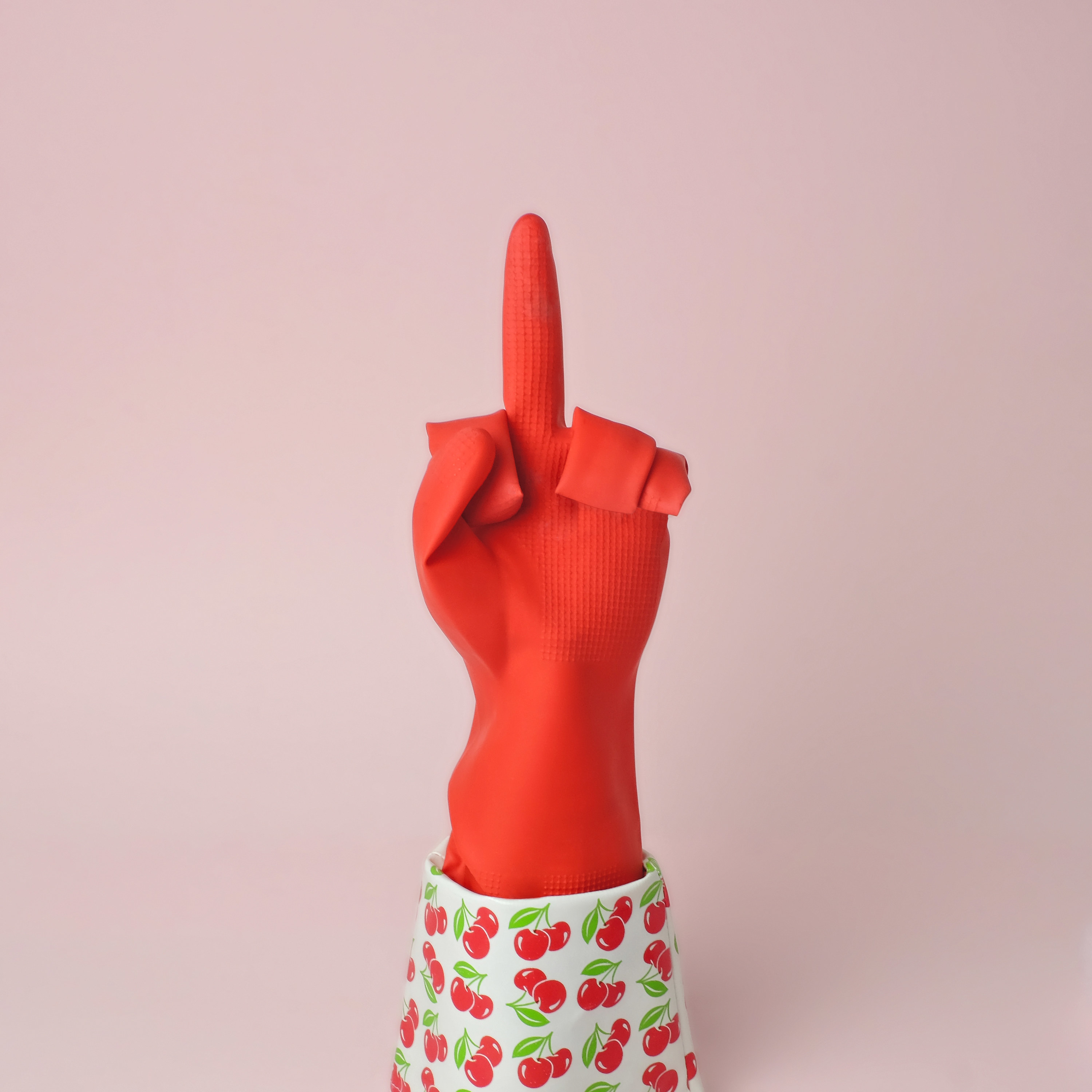Rubber dishwashing glove with cherries decorating the end, stood up on end with fingers arranged with middle finger up