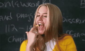 cher from a scene in clueless in front of a chalk board twisting her gum with her finger