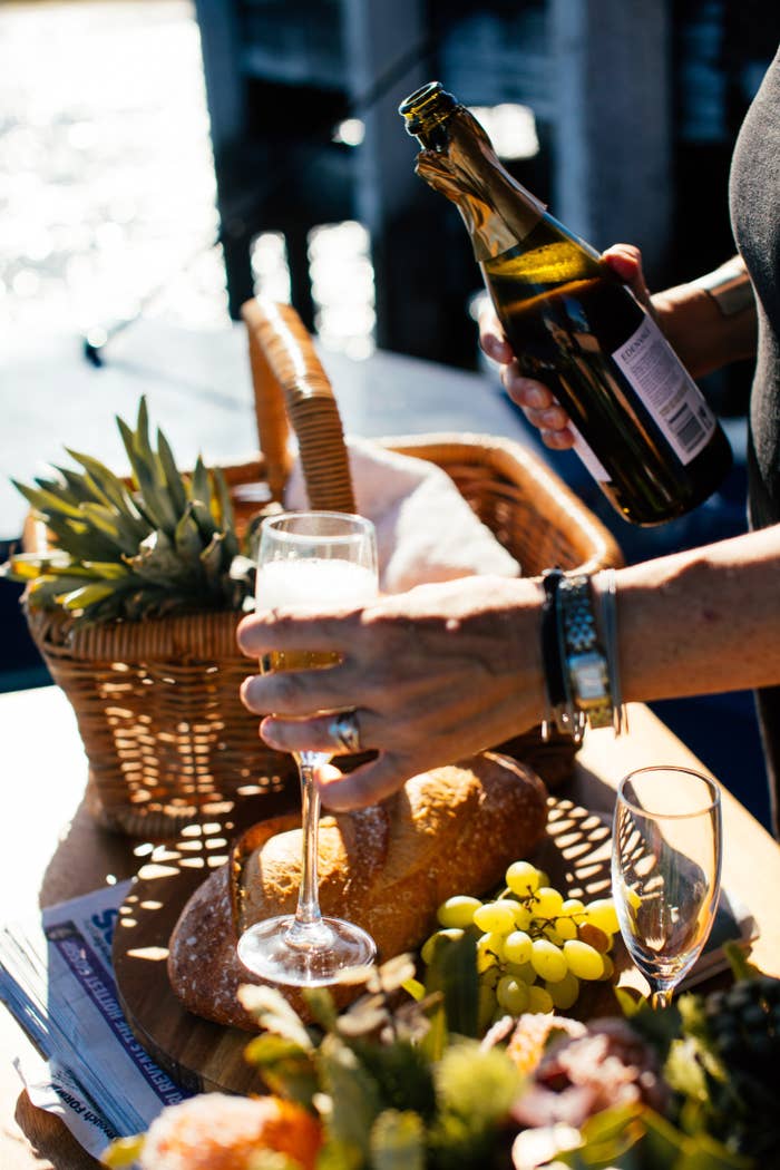 Someone pours champagne into a flute with a fun charcuterie spread.