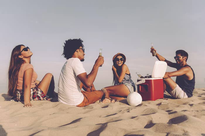 A group of friends sitting on the beach with a full cooler.
